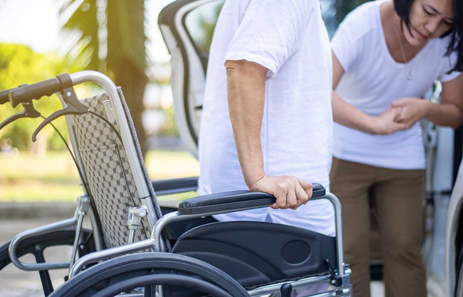 Woman helping man out of wheelchair.