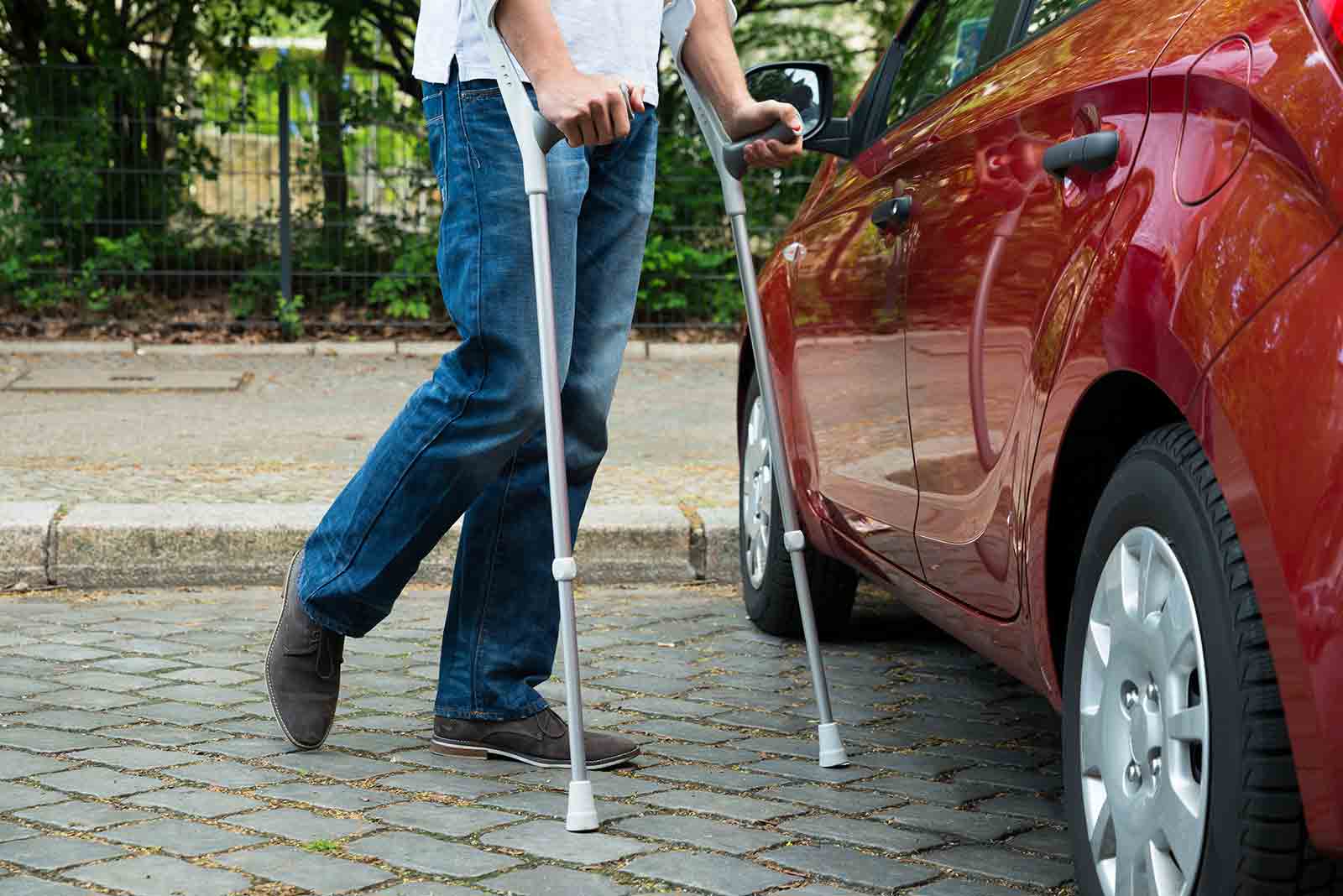 Man with crutches walking to car.