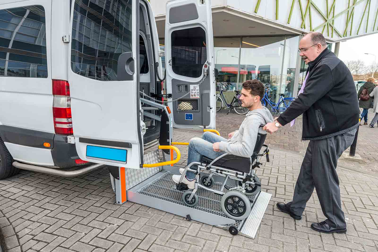 Man in wheelchair being pushed onto wheelchair van lift.